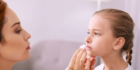 Sad girl with nose injury standing in front of her mother.