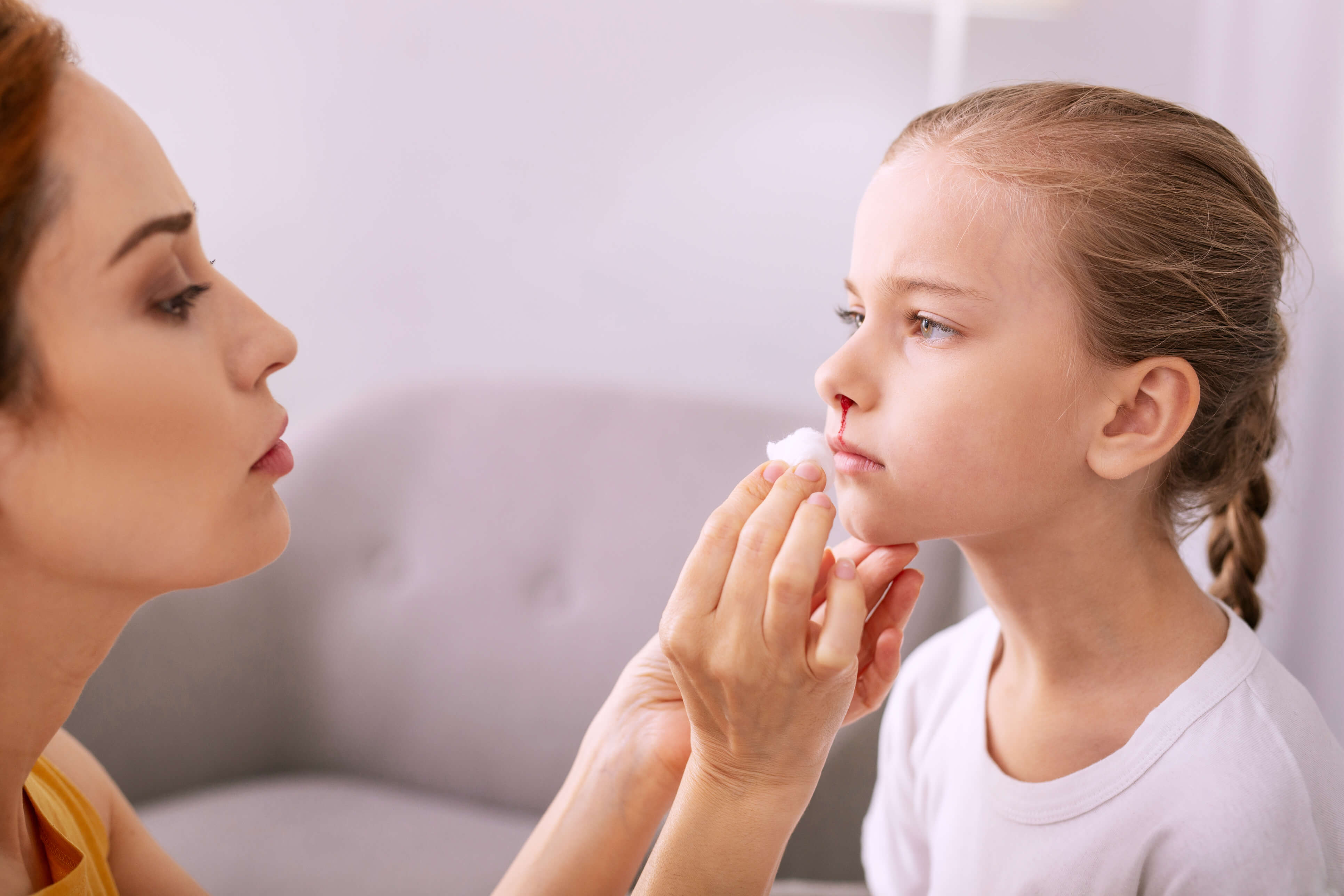 Sad girl with nose injury standing in front of her mother.